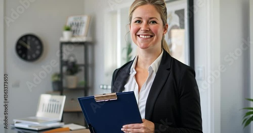 Professional woman at office holding clipboard while smiling during meeting at modern workspace