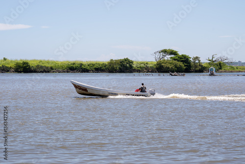 Canvas-taulu persona trasladándose en lancha de motor por el mar con fondo de vegetación