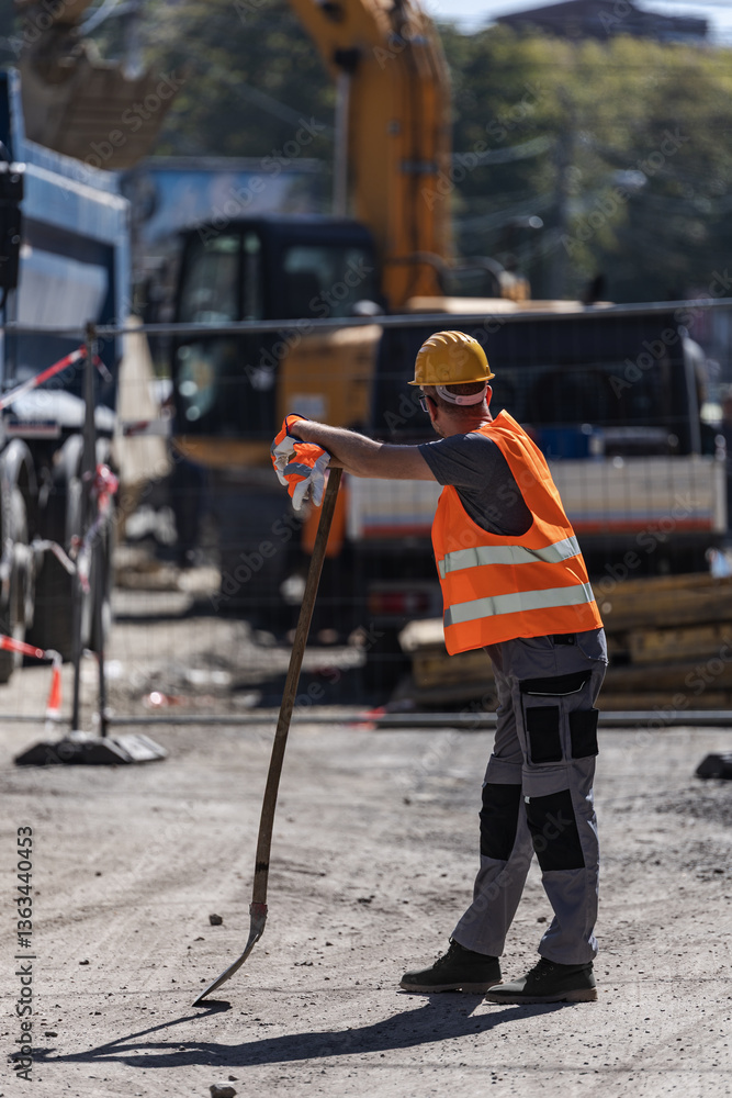 Naklejka premium Construction worker using a tool for site preparation during the day near heavy machinery and equipment