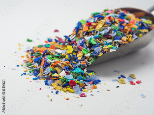 Various colors of plastic waste that has been ground in a stainless shovel on a white background
