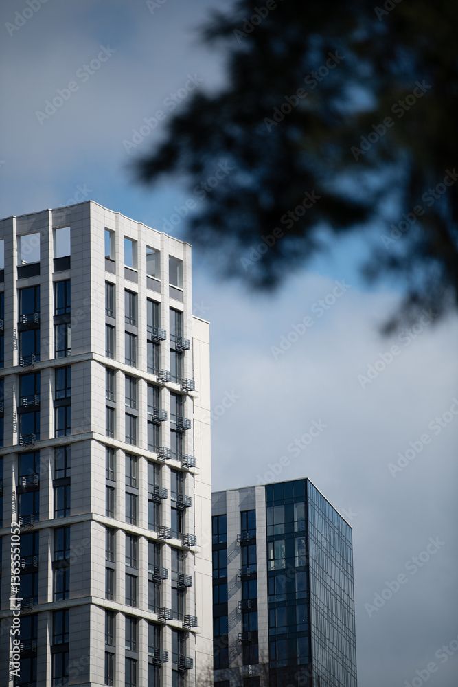 Two towering modern buildings feature striking designs, standing tall under a cloudy sky in an urban landscape. The structures display a mix of glass and concrete elements Two towering modern buildings feature striking designs, standing tall under a cloudy sky in an urban landscape. The structures display a mix of glass and concrete elements