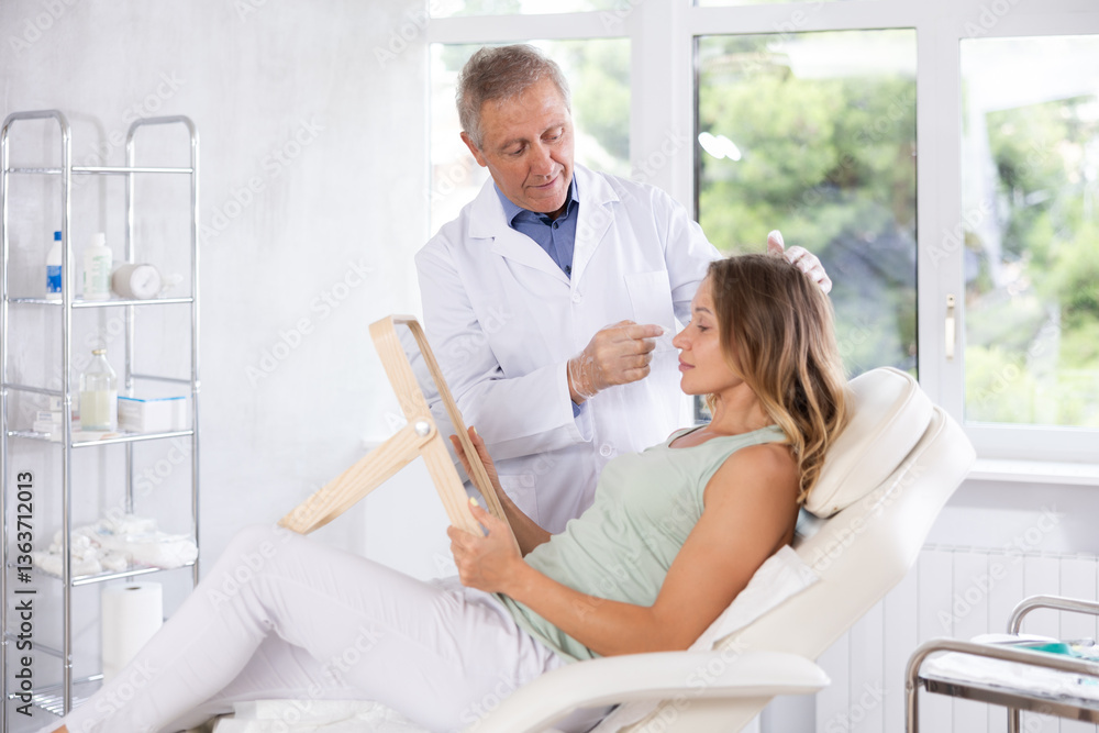 Obraz premium Old male doctor consulting middle-aged woman patient lying on clinical chair in beauty clinic