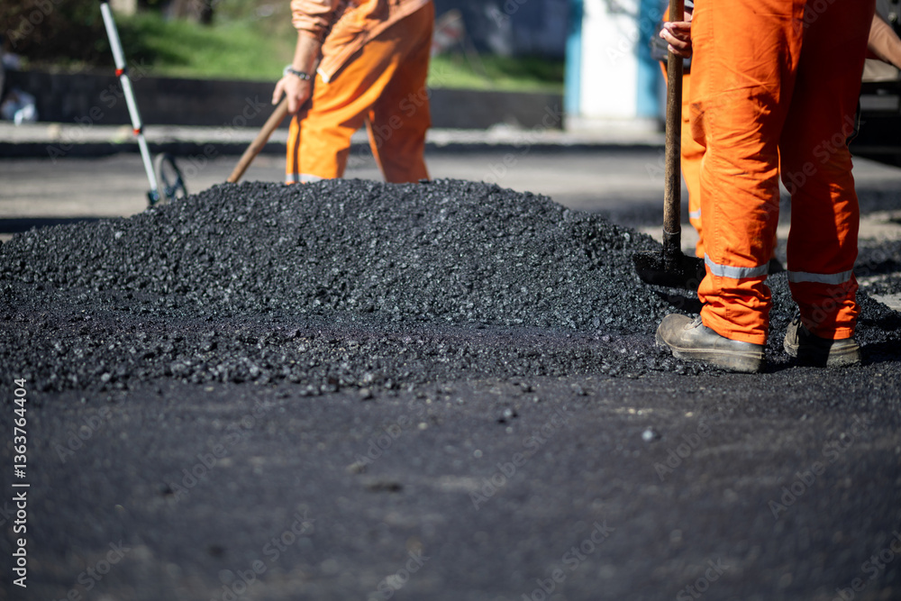 Road construction workers laying asphalt at a street repair site during daylight hours in an urban setting Road construction workers laying asphalt at a street repair site during daylight hours in an urban setting