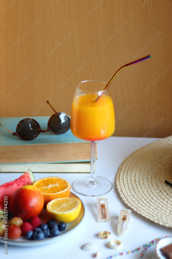 Glass of cocktail, straw hat, sunglasses, books, fresh fruit, chocolate and accessories. Summer essentials on the table. Selective focus.