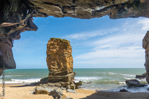 View of stone monolith and beach from inside a cave
