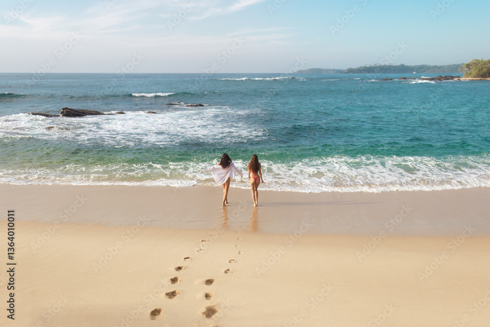 Two women walk hand-in-hand towards the ocean on a serene Sri Lankan beach, leaving footprints in the sand. The peaceful scene captures the beauty of a tropical getaway, perfect for themes of travel Two women walk hand-in-hand towards the ocean on a serene Sri Lankan beach, leaving footprints in the sand. The peaceful scene captures the beauty of a tropical getaway, perfect for themes of travel