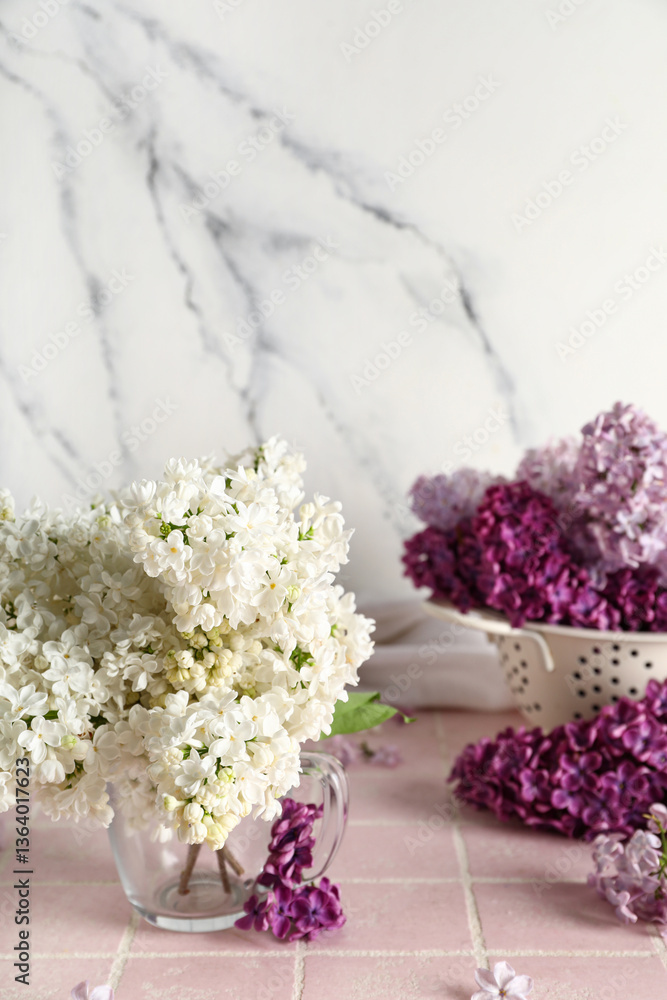 Obraz premium Colander and cup of beautiful fragrant lilac flowers on pink tile near grunge white background