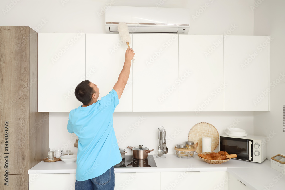Young man cleaning air conditioner with pp-duster in kitchen, back view Young man cleaning air conditioner with pp-duster in kitchen, back view