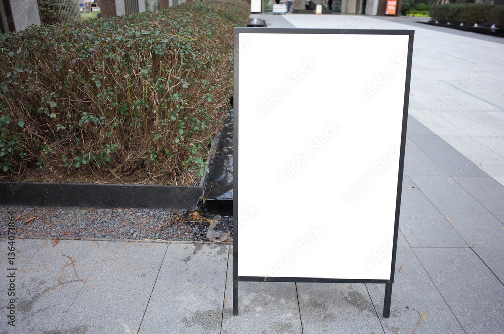 Blank white outdoor advertising stand or sandwich board mock up template. Clear street signage board placed by an outdoor dinning area of a restaurant. Background texture of standee on street.