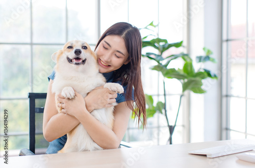 Obraz na płótnie Asian young beautiful woman happy smile sitting hugging her beloved cute welsh corgi dog on chair working using computer in living room at home Love pet animals leisurely best friend lifestyle balance w salonie