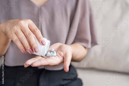 close up of woman's hand holding a bottle of medicine while taking vitamin pills or supplements such as probiotics, zinc, or magnesium to support her health and well being