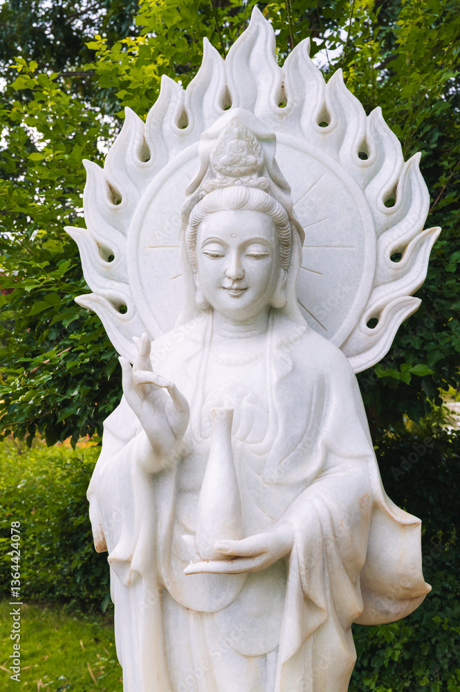 Fototapeta premium White Buddha statue surrounded by tropical plants in a garden in Asia.