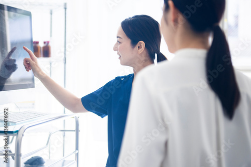 Obraz na płótnie A female doctor in blue scrubs is smiling and pointing at a medical monitor while explaining results to a patient in a clinical setting. w salonie