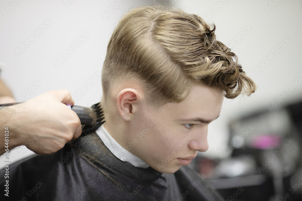 Fototapeta premium man is cutting a boy's hair in a barbershop. The boy is sitting in a chair while the man works on his hair. The atmosphere is casual and relaxed