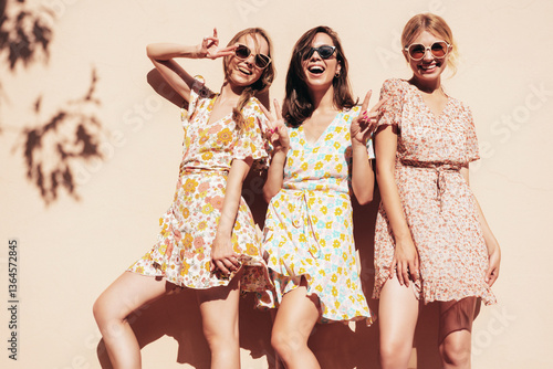 Three young beautiful smiling hipster female in trendy summer dress clothes. Sexy carefree women posing in the street. Positive models having fun outdoors at sunny day. Cheerful and happy. Near wall