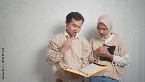 Two young adults reviewing documents together, one wearing a hijab, both facing a document.