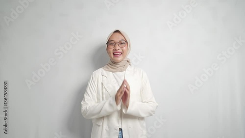 A young asian woman with glasses and a hijab poses in a white blazer.