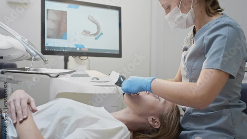 Doctor woman makes a 3d scan of the teeth of a female patient. Creates a 3D model of the jaw, heals the mouth. Dental clinic. Uses a smart device oral cavity scanner on the monitor.