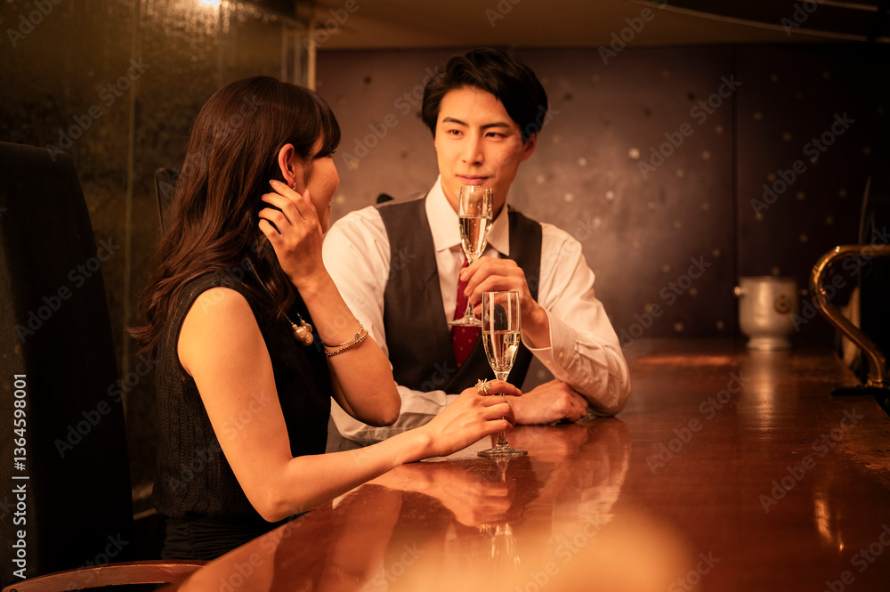 A couple dressed in formal attire clinks champagne glasses in a warm, romantic bar setting. Their smiles reflect joy and connection, emphasizing a mood of celebration.