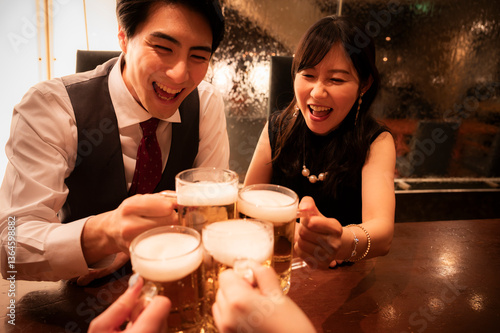 A group of friends raises their beer mugs in a lively toast around a wooden table in a bar. Everyone is laughing and smiling, sharing a fun and festive moment together.