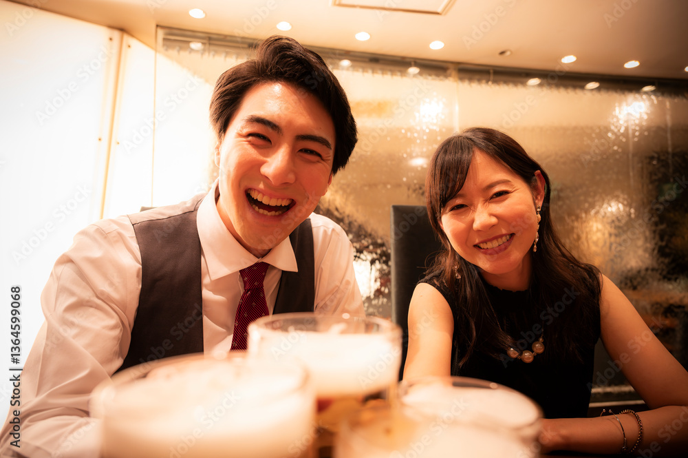A smiling couple raises their glasses of beer with friends in a bright, warmly lit bar. The mood is festive and welcoming, full of laughter and joy.