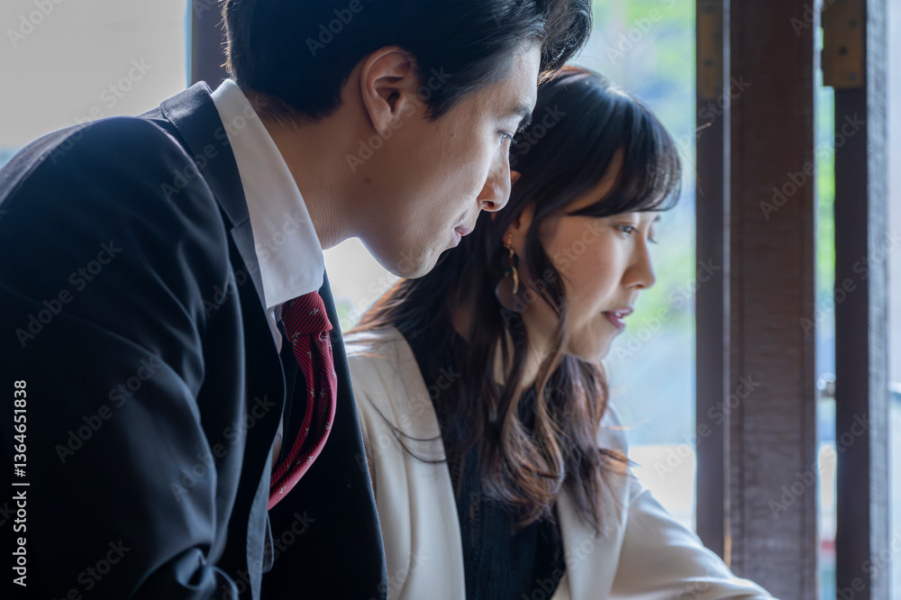 A businessman and a businesswoman in formal attire have a serious conversation while seated by the window at a modern café. Natural light highlights their focused expressions as they engage in a profe