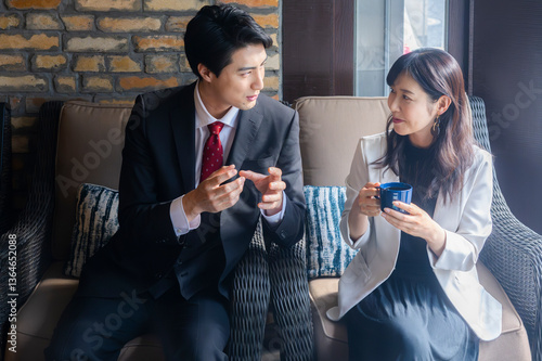 Obraz na płótnie A businessman in a dark suit and red tie gestures while speaking with a female colleague in a light blazer during a strategic meeting in a cozy café with a brick wall background. w salonie