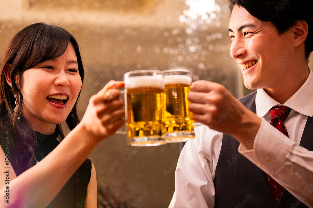 A joyful man and woman clink their beer mugs together in a celebratory toast at a warmly lit bar. Both are smiling brightly, creating a cheerful and relaxed atmosphere.