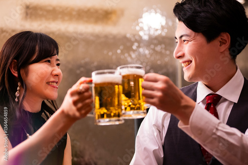 Obraz na płótnie A joyful man and woman clink their beer mugs together in a celebratory toast at a warmly lit bar. Both are smiling brightly, creating a cheerful and relaxed atmosphere. w salonie