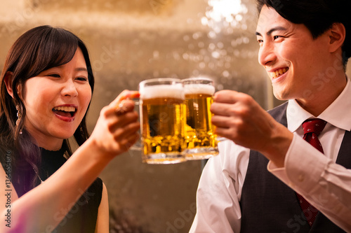 Obraz na płótnie A joyful man and woman clink their beer mugs together in a celebratory toast at a warmly lit bar. Both are smiling brightly, creating a cheerful and relaxed atmosphere. w salonie