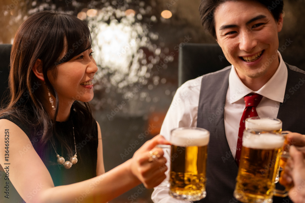 A smiling man and woman enjoy a moment of celebration with beer at a sleek bar. The man wears a white shirt with a red tie and vest, and the woman smiles warmly as they toast.