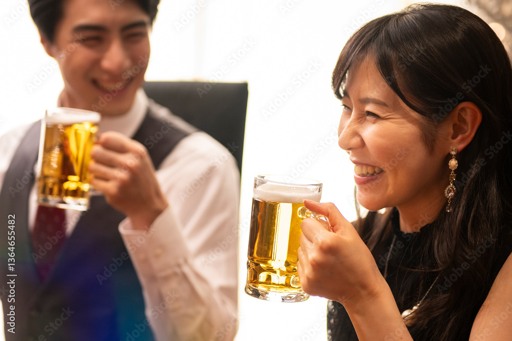 A smiling woman dressed elegantly in black raises her beer mug in a cheerful toast at a warmly lit bar. Her pearl necklace and statement earrings add a touch of luxury to the lively, social atmosphere