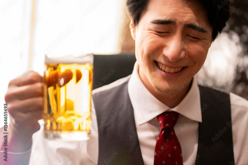 A cheerful man in formal attire smiles with his eyes closed while holding a large glass mug of beer. The scene is warmly lit, capturing a joyful and relaxed moment in a stylish bar setting.
