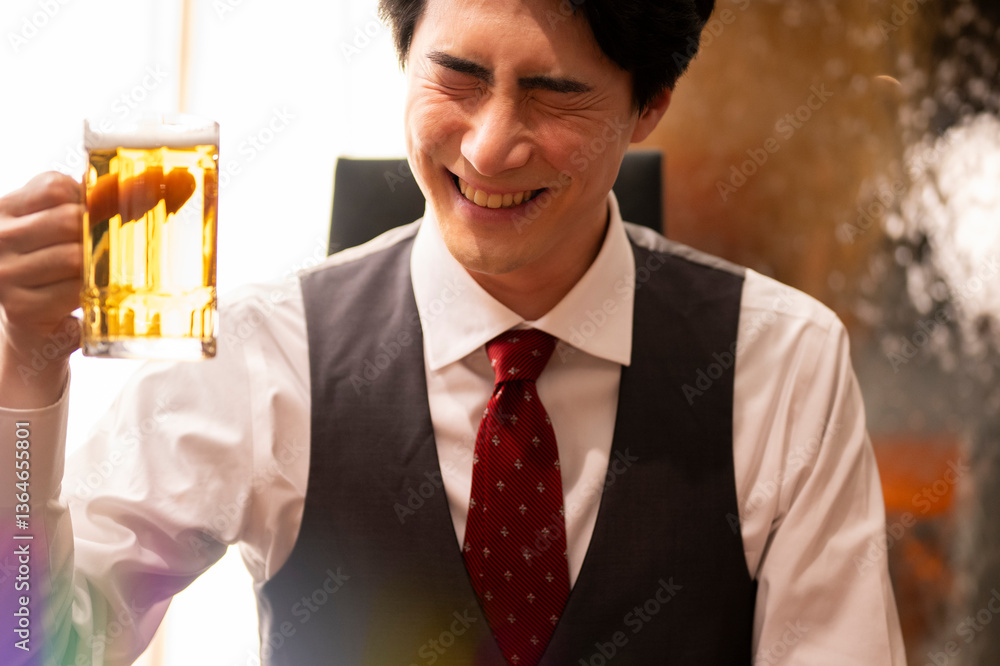A cheerful man in formal attire smiles with his eyes closed while holding a large glass mug of beer. The scene is warmly lit, capturing a joyful and relaxed moment in a stylish bar setting.