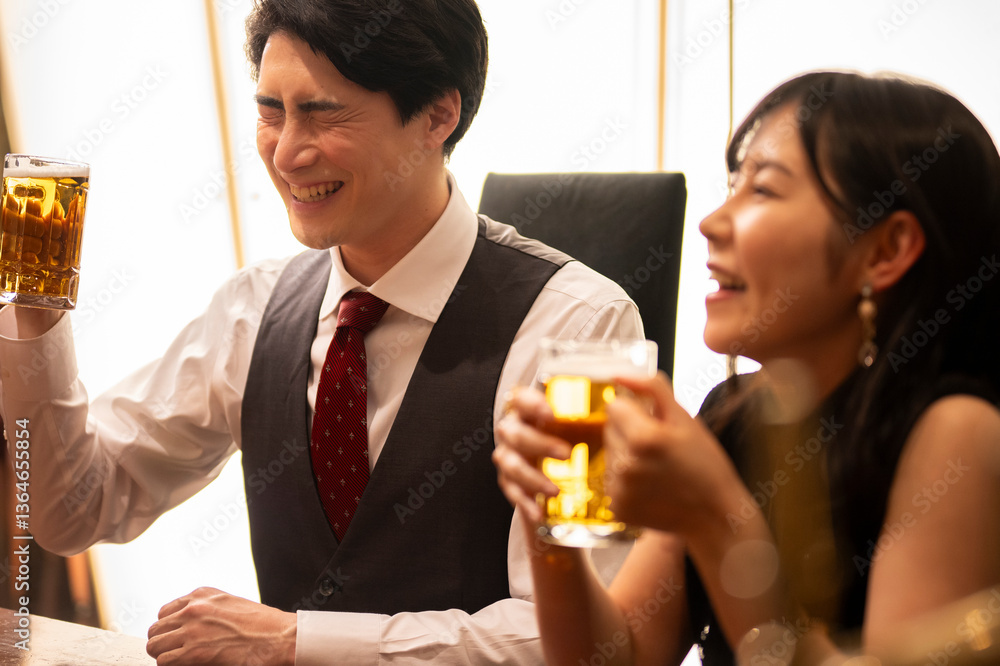 A man and woman sit side by side in a stylish bar, laughing and enjoying a drink together. Both are holding mugs of beer, and the mood is lighthearted and full of camaraderie, suggesting a casual date