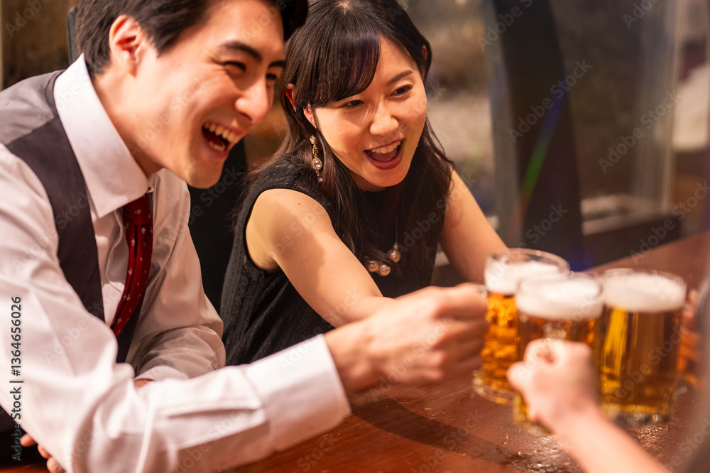 A joyful group of 4 friends toasts with beer mugs while sitting at a polished wooden bar. The ambient lighting and formal clothing suggest a special celebration or social gathering.