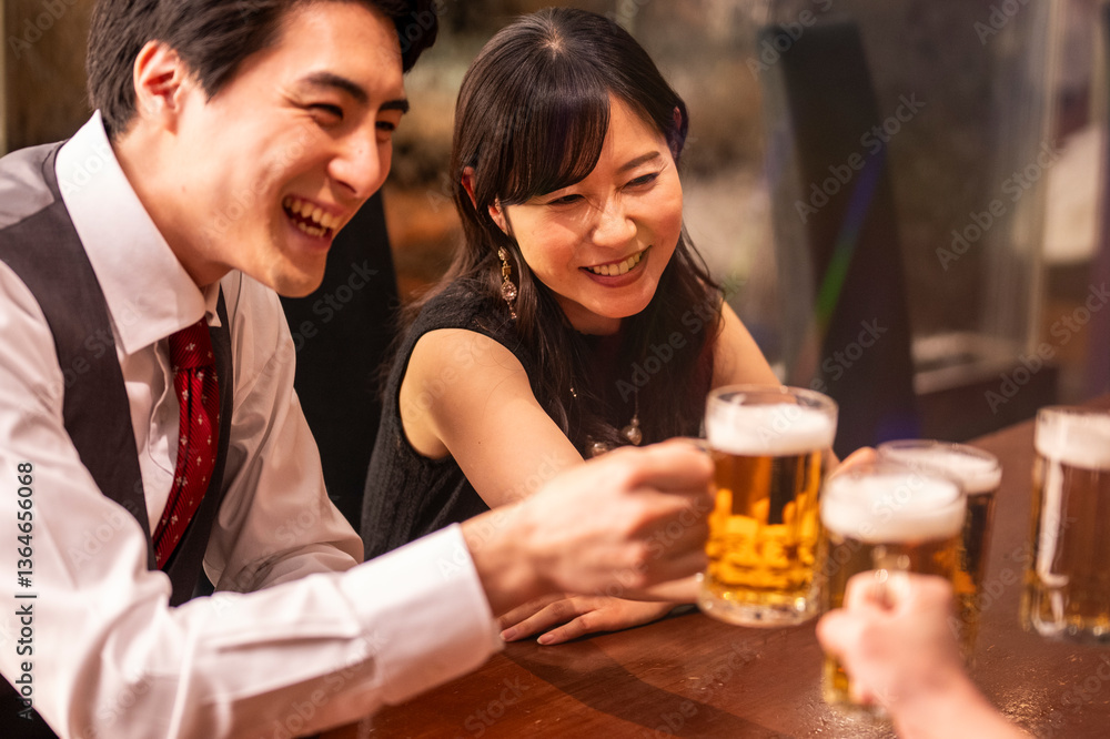 A joyful group of 4 friends toasts with beer mugs while sitting at a polished wooden bar. The ambient lighting and formal clothing suggest a special celebration or social gathering.