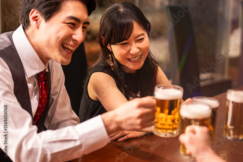 Obraz na płótnie A joyful group of 4 friends toasts with beer mugs while sitting at a polished wooden bar. The ambient lighting and formal clothing suggest a special celebration or social gathering. w salonie