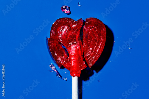 Broken heart-shaped lollipop on a blue background symbolizing heartbreak