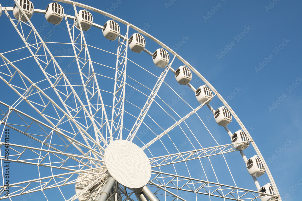 Part of white Ferris wheel against blue sky on cloudless summer day. Outdoors. Amusement park.