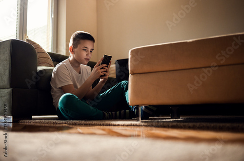 Boy sitting on floor at home using smart phone typing message to a friend.