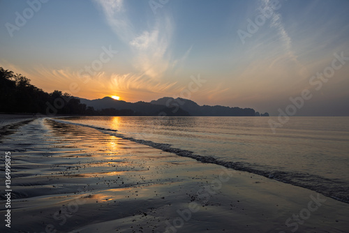 Wallpaper Mural Tranquility.  Sunrise over a headland on a sandy beach in Thailand. The sea is calm with gentle ripples and the wet sand reflects the golden sunlight. Wispy clouds in the blue sky. Torontodigital.ca