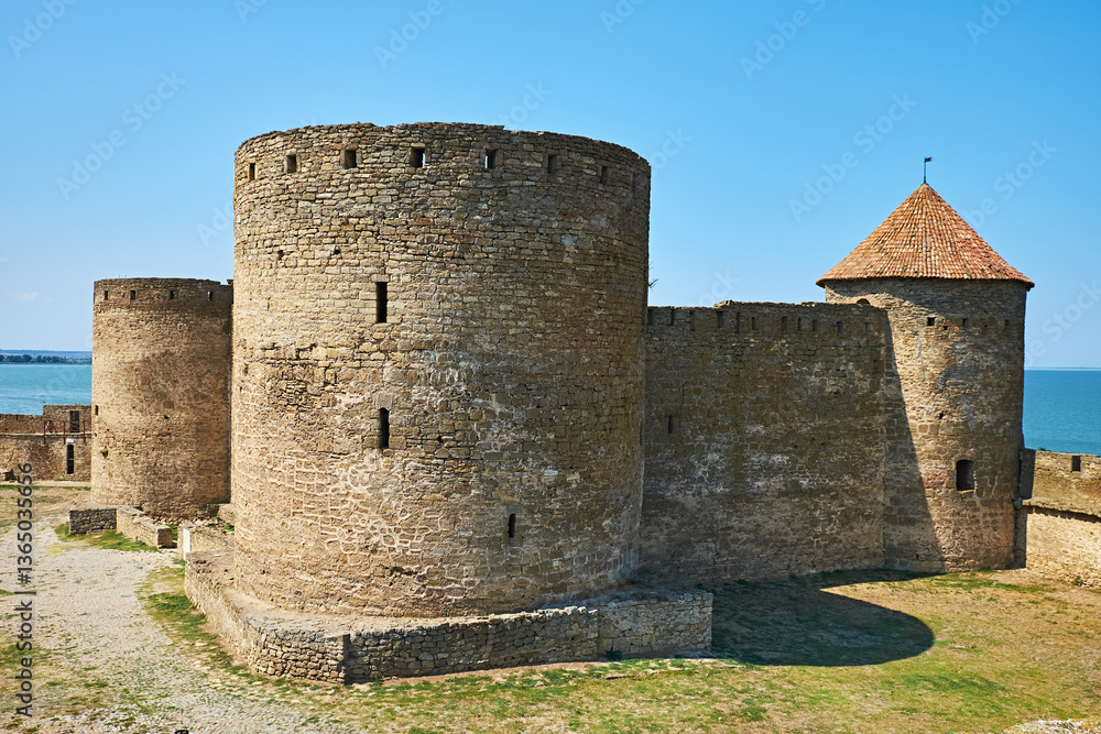 Ancient medieval fortress with massive stone towers near the sea under a clear blue sky. Ancient medieval fortress with massive stone towers near the sea under a clear blue sky.
