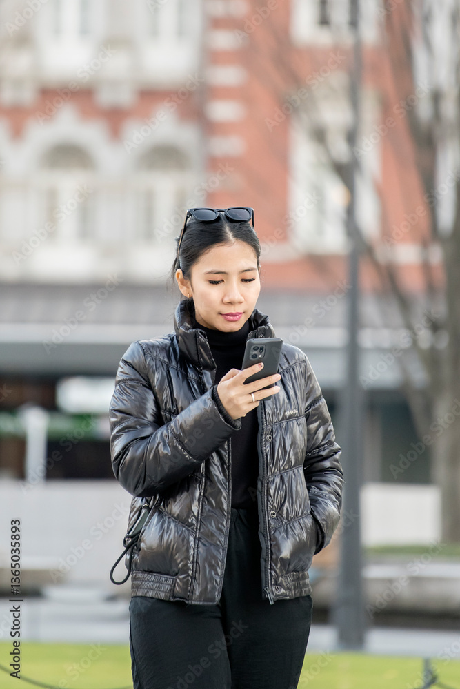 Fototapeta premium Young Woman in Stylish Winter Outfit Using Smartphone in Urban Setting