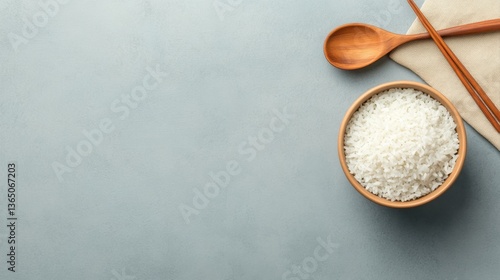 Bowl of white rice on a textured surface with wooden spoon and chopsticks, minimalistic kitchen setting for food photography and culinary use