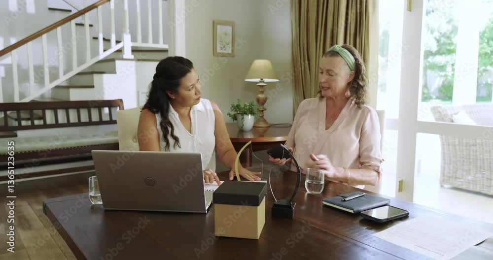 Senior diverse women at home laughing and using smartphone together at dining table Senior diverse women at home laughing and using smartphone together at dining table
