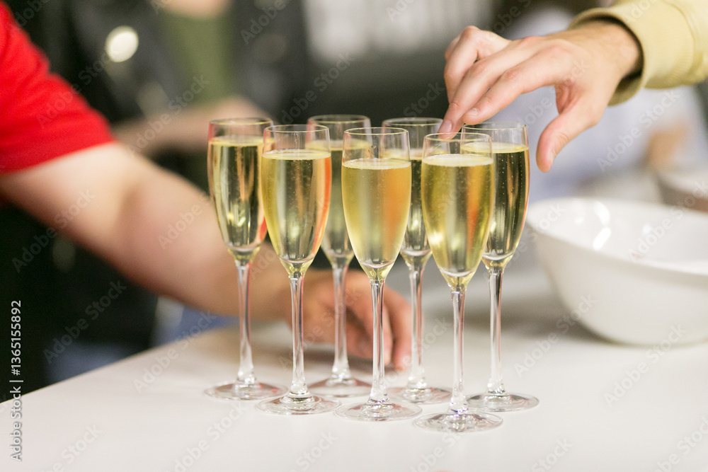 Obraz premium A person extends their hand towards a glass of champagne on a table