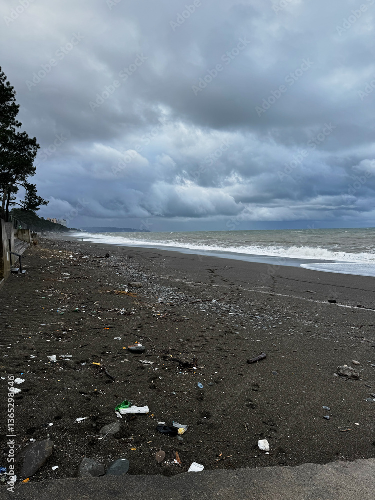 Polluted black sand beach with ocean waves under a stormy sky