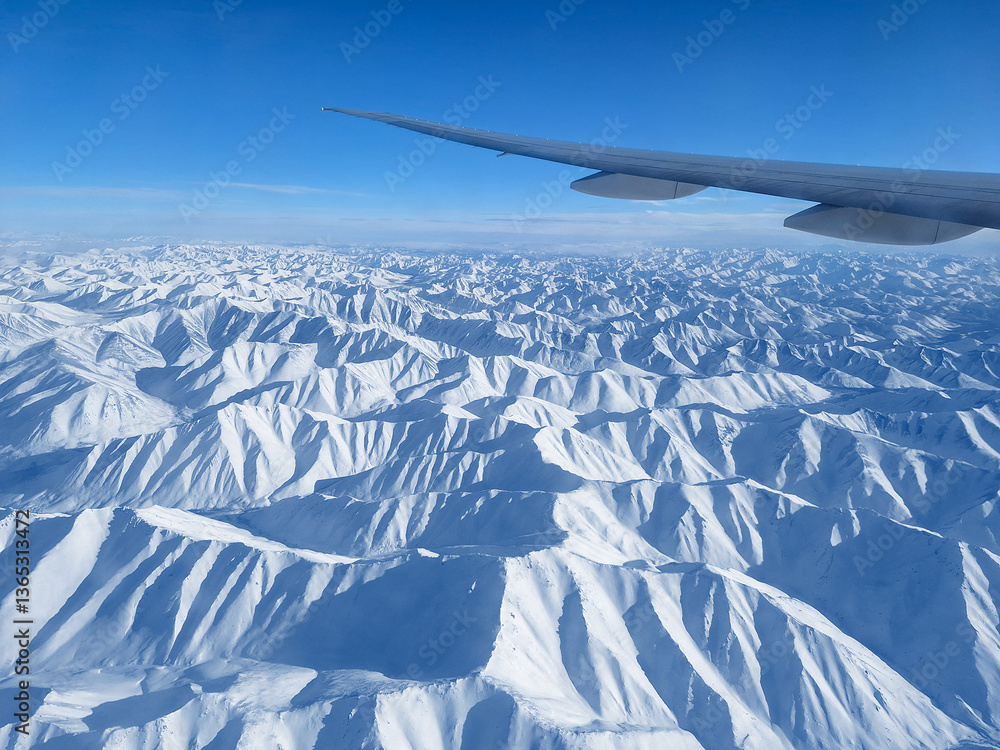 View from a flying airplane on snow-capped mountains and an airplane wing. Beautiful winter mountain landscape. Flight on a passenger plane over a mountainous area. Aviation tourism and travel.
