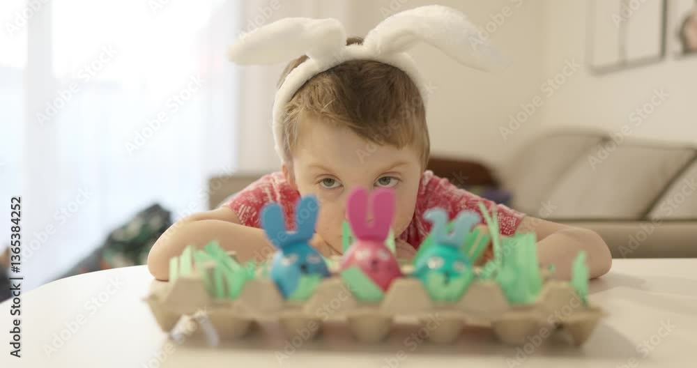 A joyful child wearing adorable bunny ears happily engaged with colorful bunny decorations on a table A joyful child wearing adorable bunny ears happily engaged with colorful bunny decorations on a table